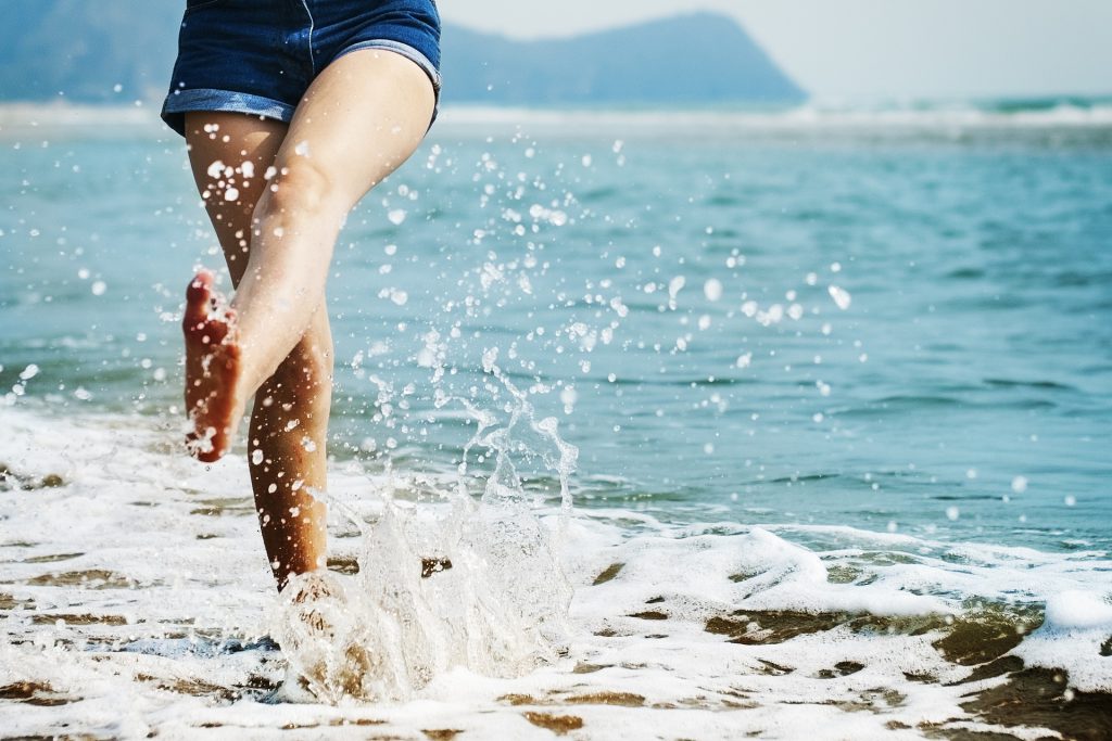 Eine Frau läuft barfuss am Strand und spritzt mit den Füßen Wasser hoch